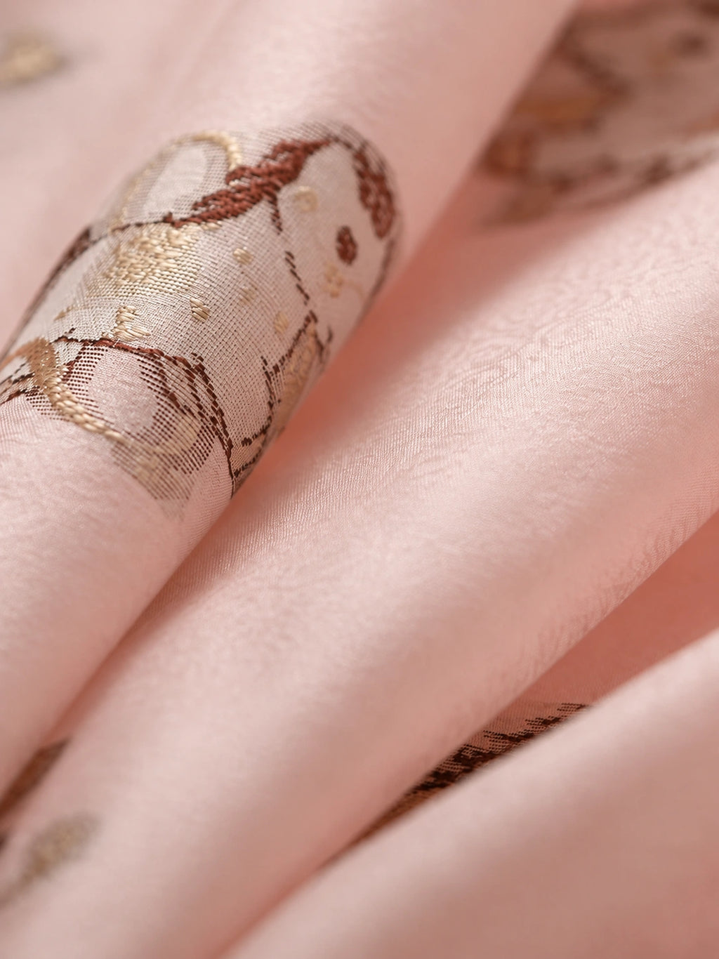 Close-up of lustrous blush pink mulberry silk fabric with woven pony motifs in brown and champagne tones