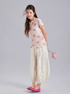 Model wearing a blush pink Gambiered Silk pony-print mulberry silk top with ivory wide-leg trousers