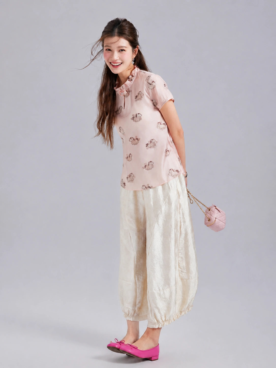 Model wearing a blush pink Gambiered Silk pony-print mulberry silk top with ivory wide-leg trousers