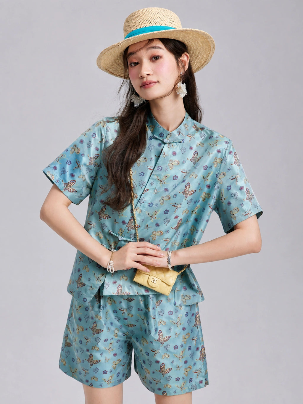 Model wearing a relaxed aqua butterfly-patterned silk shirt with matching wide-leg shorts.