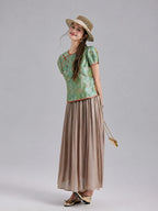 Model wearing a jade green Gambiered Silk butterfly silk top with a taupe pleated maxi skirt