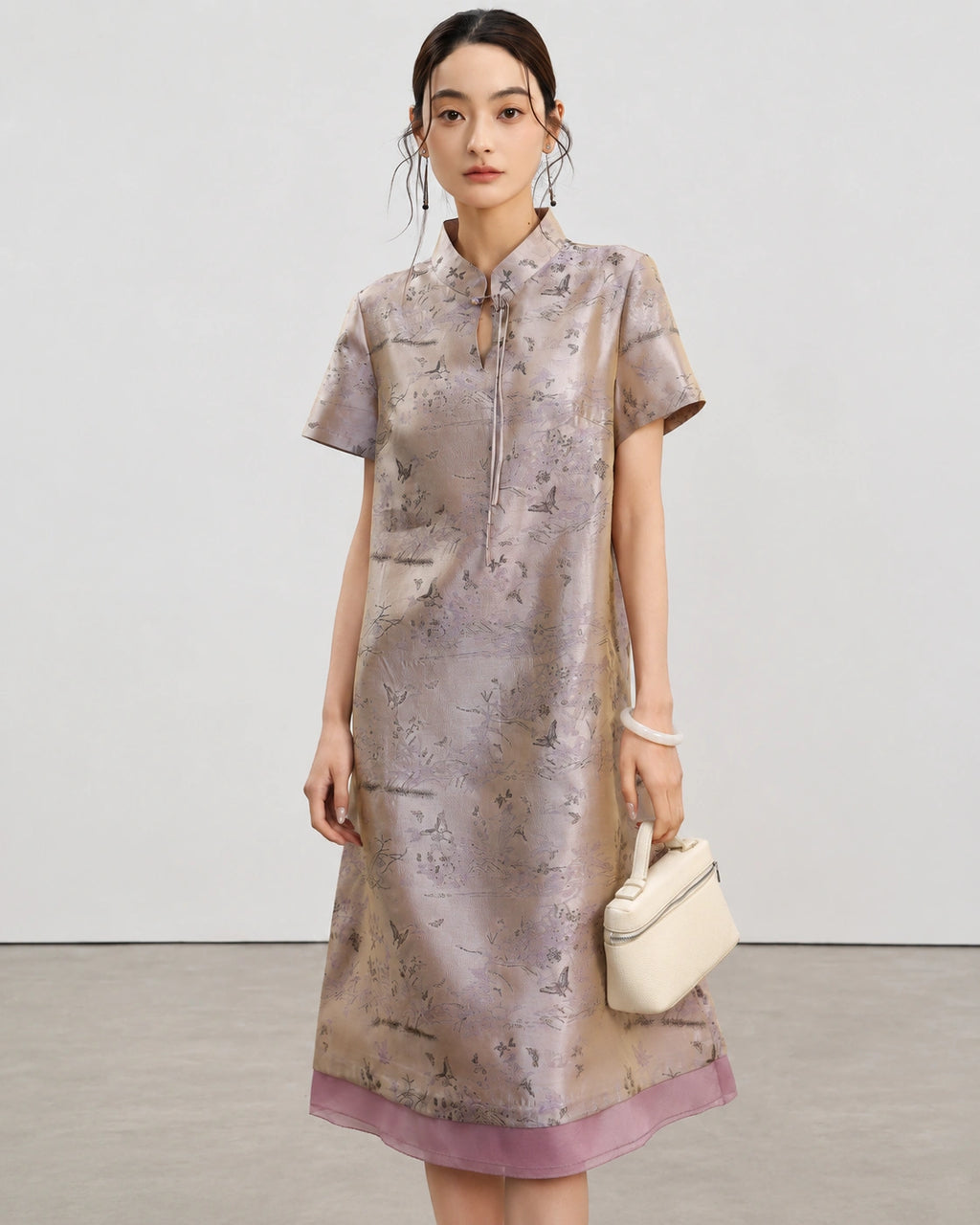 Front view of the light lavender jacquard silk A-line qipao styled with an ivory handbag