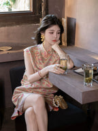 Seated model wearing a coral and champagne Shu brocade mulberry silk dress with a Mandarin collar.