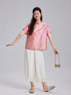 Model wearing a coral pink Gambiered Silk jacquard silk top with ivory wide-leg trousers