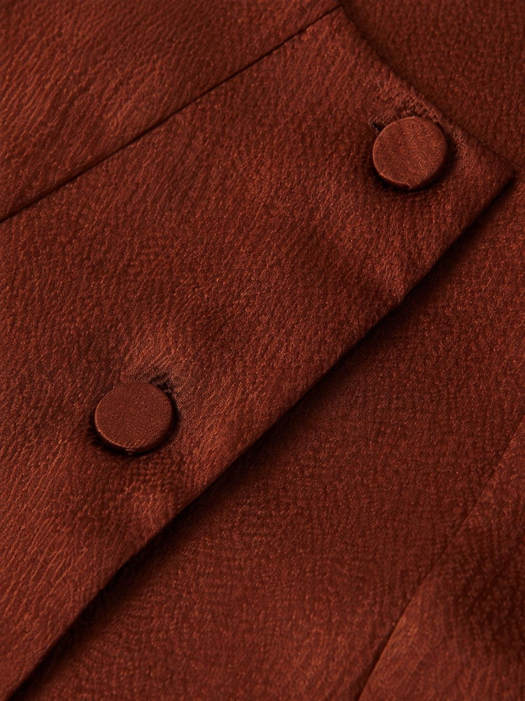 Close-up of matching silk-covered buttons and textured rust-brown mulberry silk fabric.