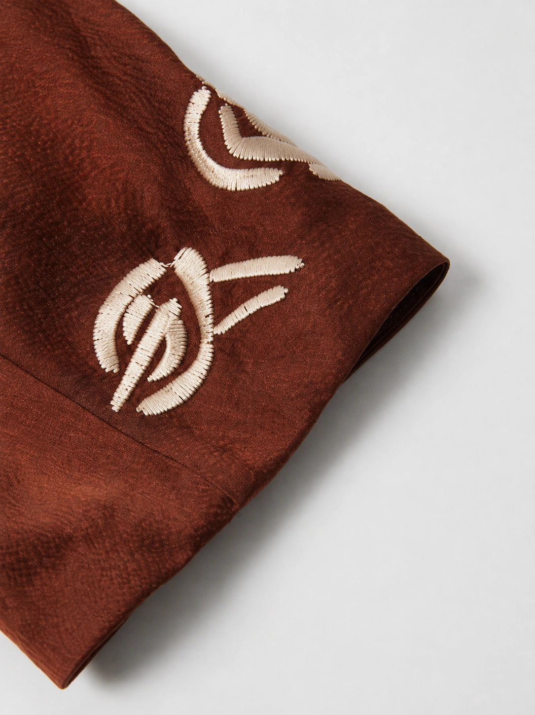 Close-up of contrasting ivory embroidery on the cuff of the rust-brown silk jacket.