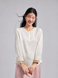Model wearing an ivory butterfly-jacquard blouse with pearl-style buttons and ornate embroidered cuffs.