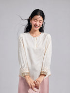 Model wearing an ivory butterfly-jacquard blouse with pearl-style buttons and ornate embroidered cuffs.