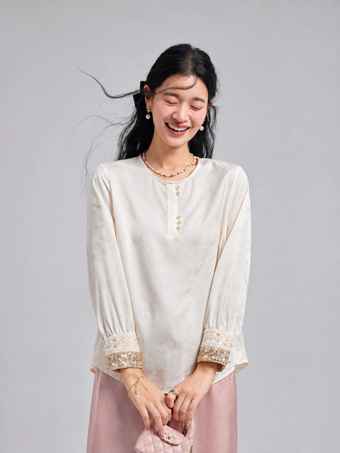 Model wearing an ivory butterfly-jacquard blouse with pearl-style buttons and ornate embroidered cuffs.