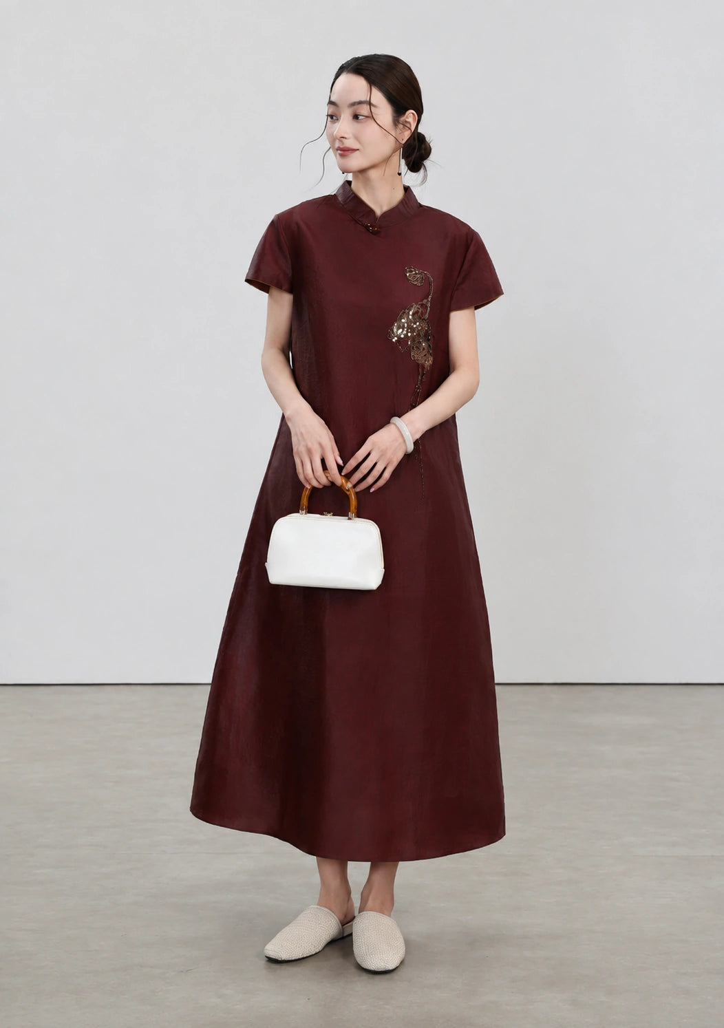 Model wearing the red embroidered silk qipao with an ivory bamboo-handle handbag