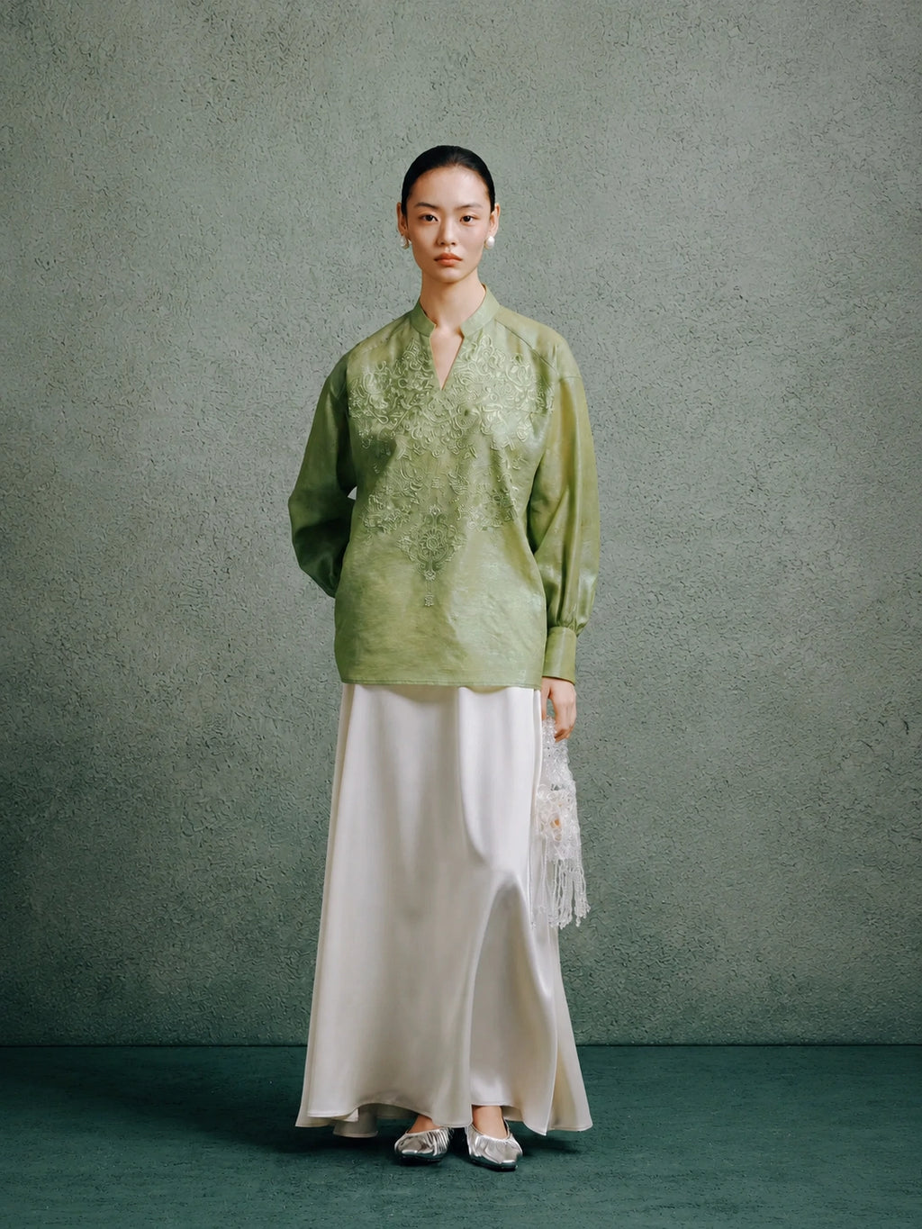 Full-length view of a woman styling a celadon green embroidered silk blouse with a flowing white skirt.