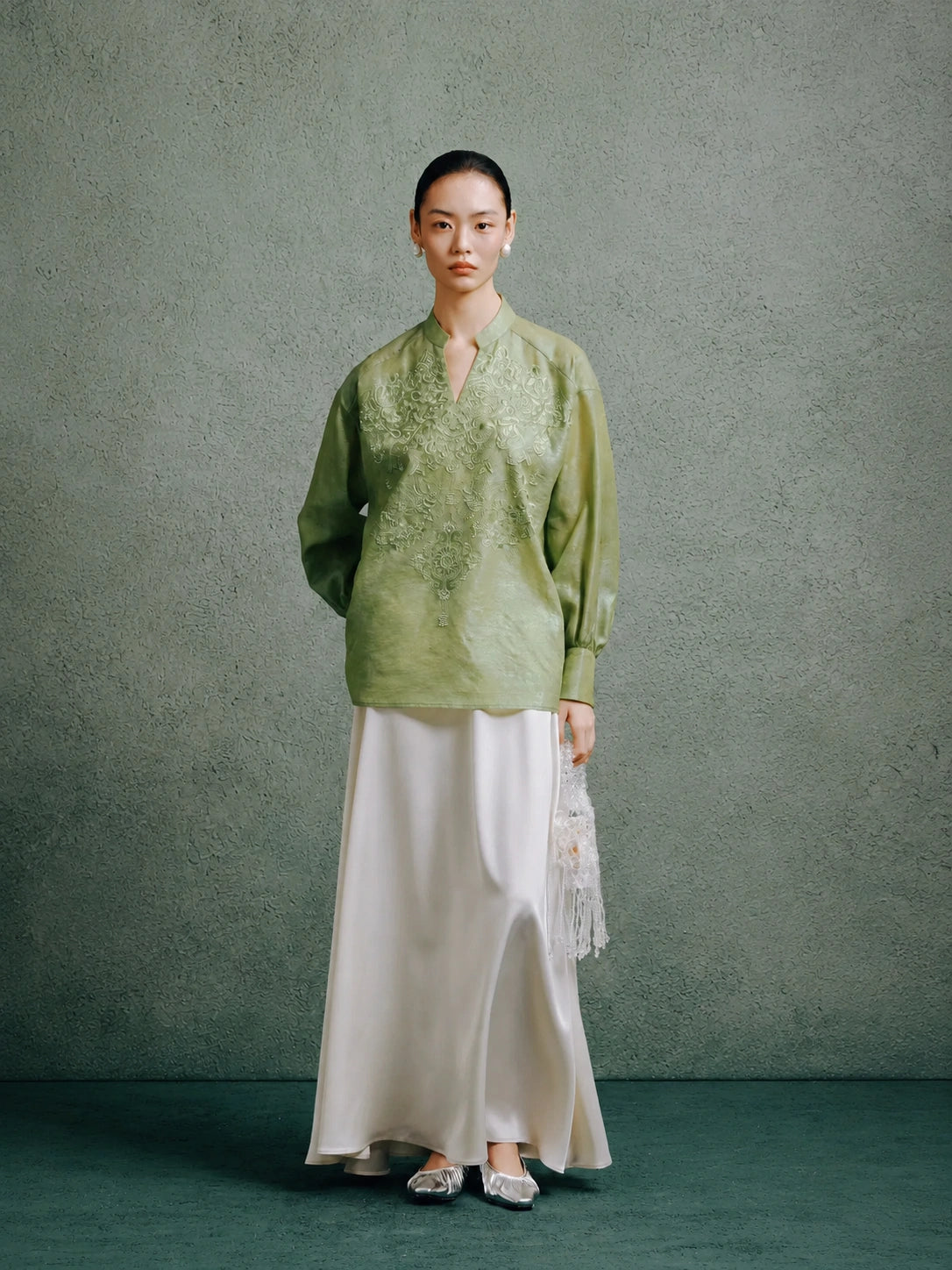 Full-length view of a woman styling a celadon green embroidered silk blouse with a flowing white skirt.