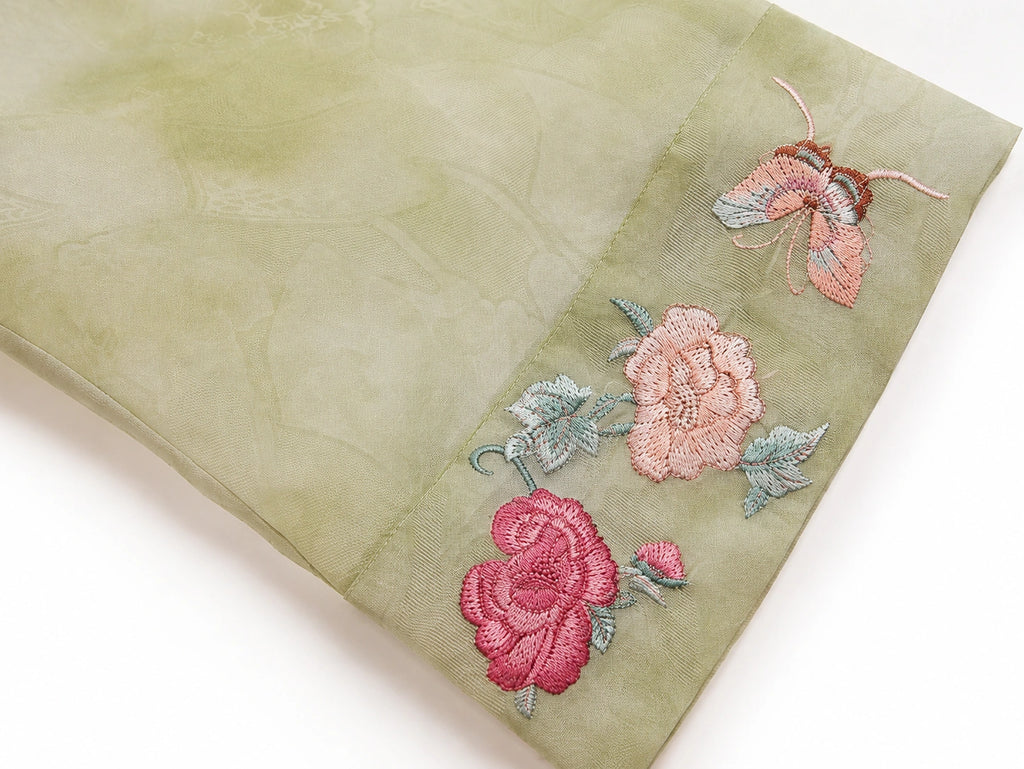 Detail of the embroidered floral cuff and tonal texture on a sage green silk overshirt