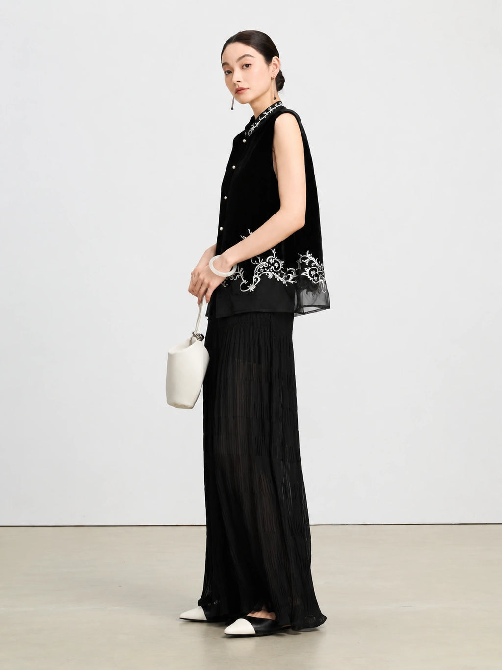 Model wearing a black embroidered silk velvet vest with a sheer hem and wide-leg trousers.