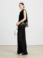 Model wearing a black embroidered silk velvet vest with a sheer hem and wide-leg trousers.
