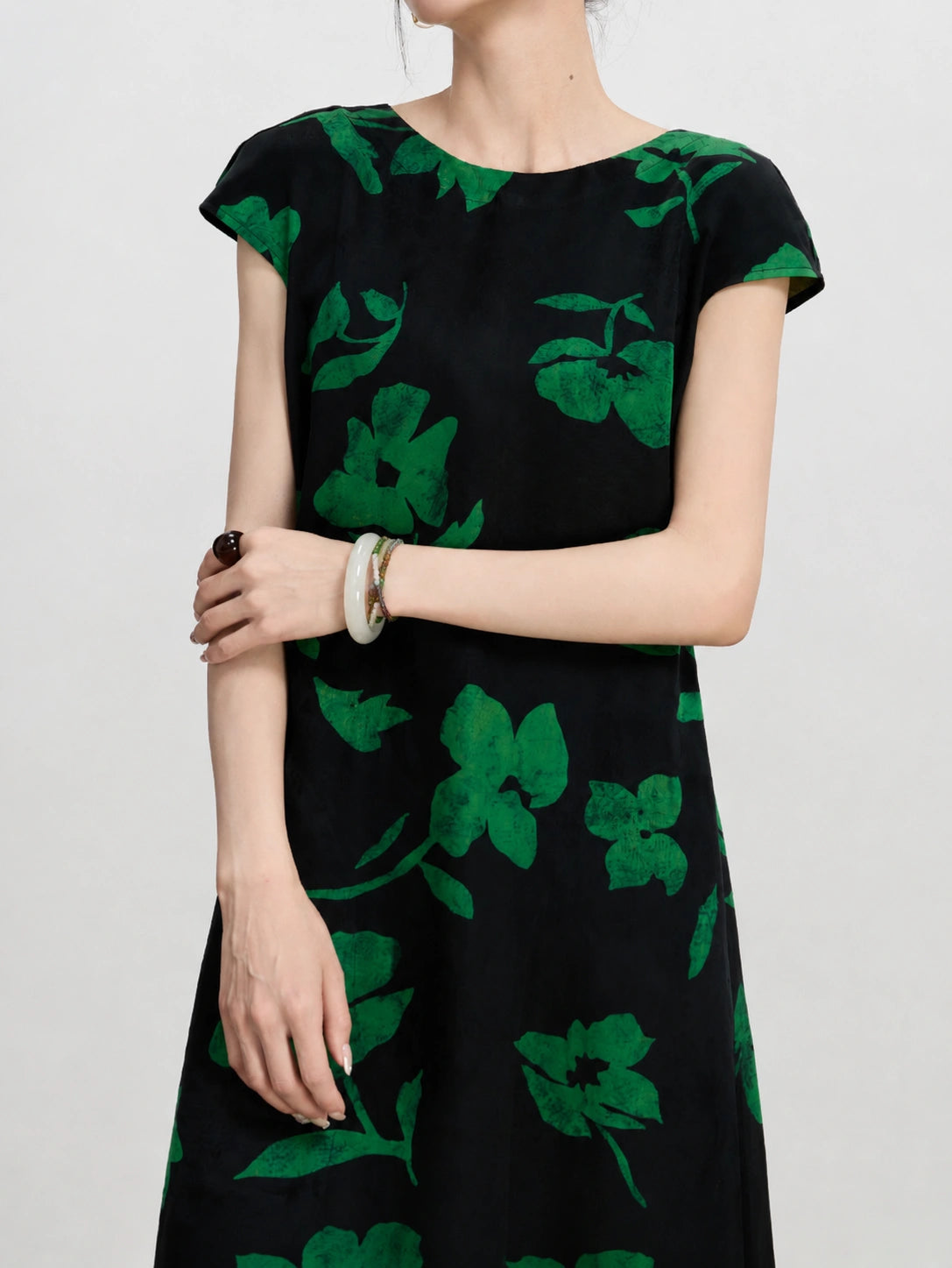 Close view of a black mulberry silk dress with emerald green floral print and cap sleeves.