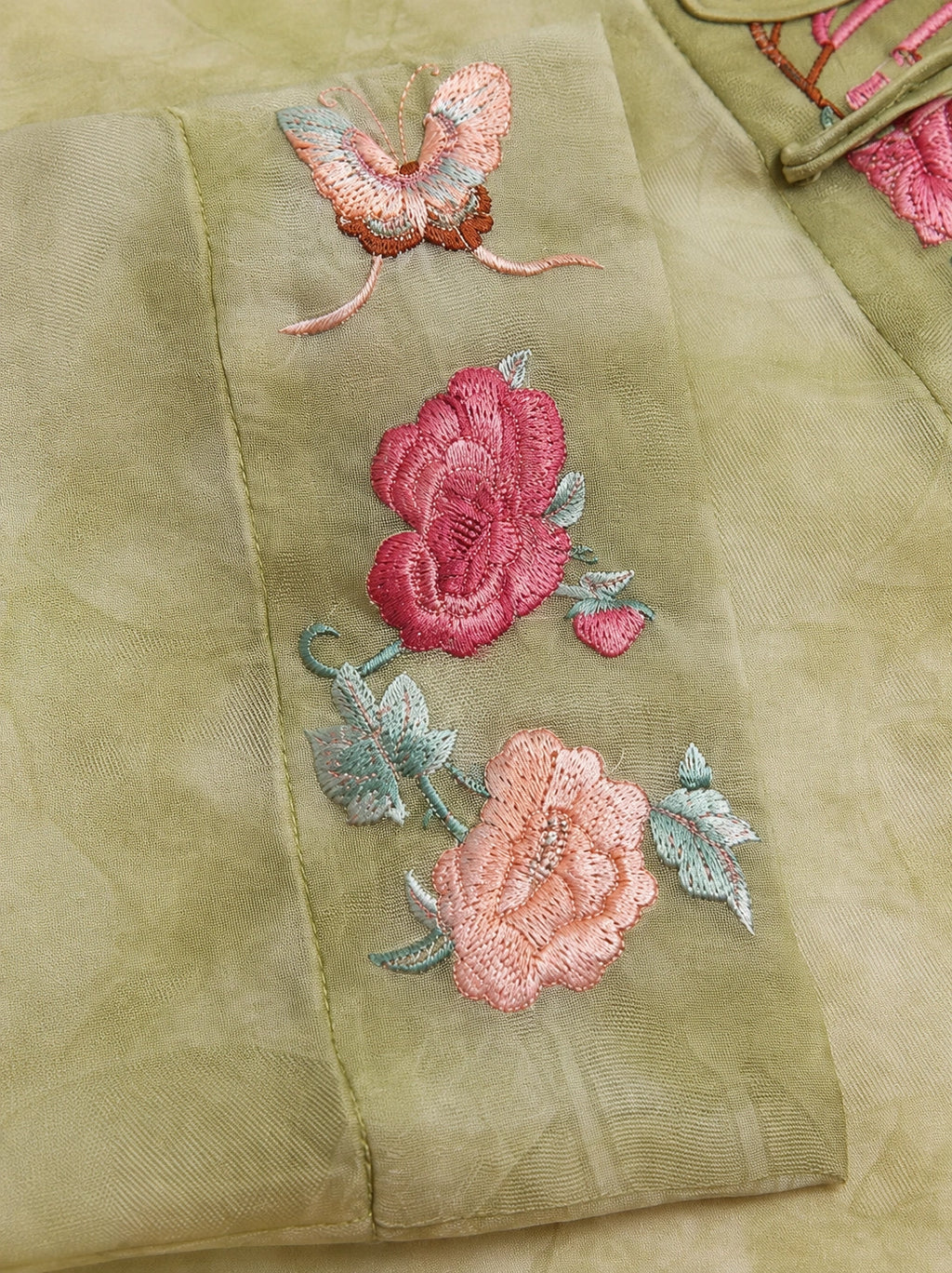 Close-up of pink floral and butterfly embroidery on a sage green silk overshirt