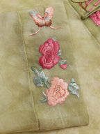 Close-up of pink floral and butterfly embroidery on a sage green silk overshirt