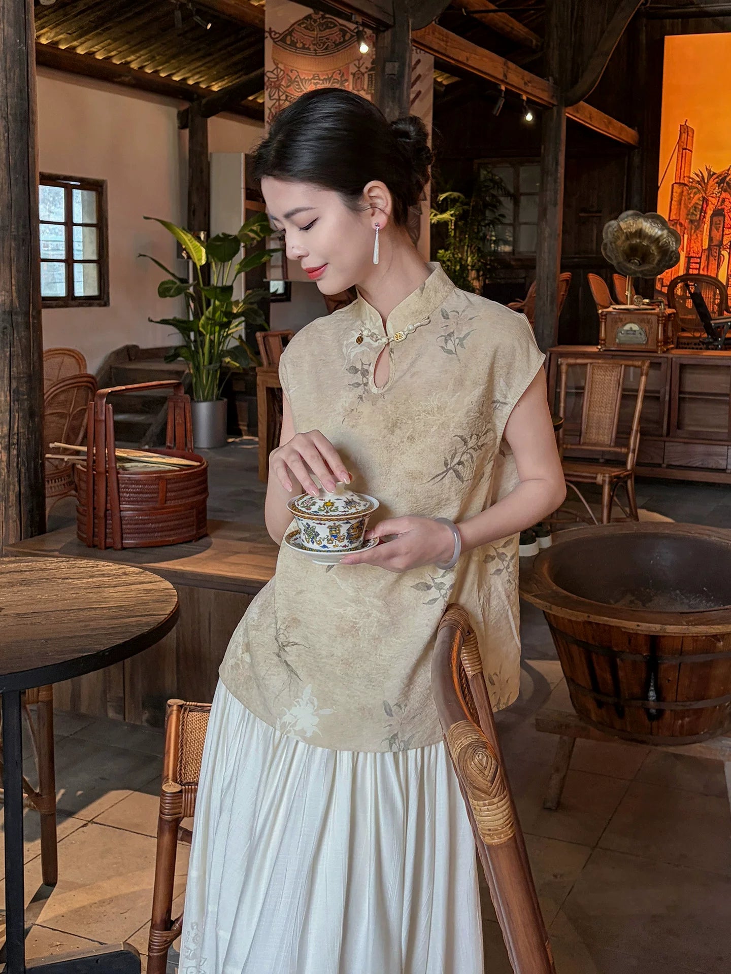 Lifestyle photo of a woman wearing the Warm Sand floral Chinese style sleeveless top in a traditional teahouse by Gambiered Silk.