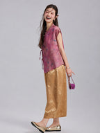 Model wearing a mulberry-rose Gambiered Silk floral top with gold wide-leg trousers.