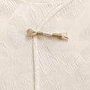 Detailed view of the decorative frog closure with gold thread and a round button