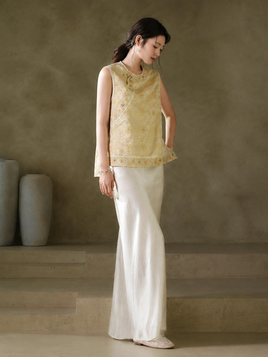 Three-quarter view of the gold jacquard vest showing its embroidered neckline and hem border