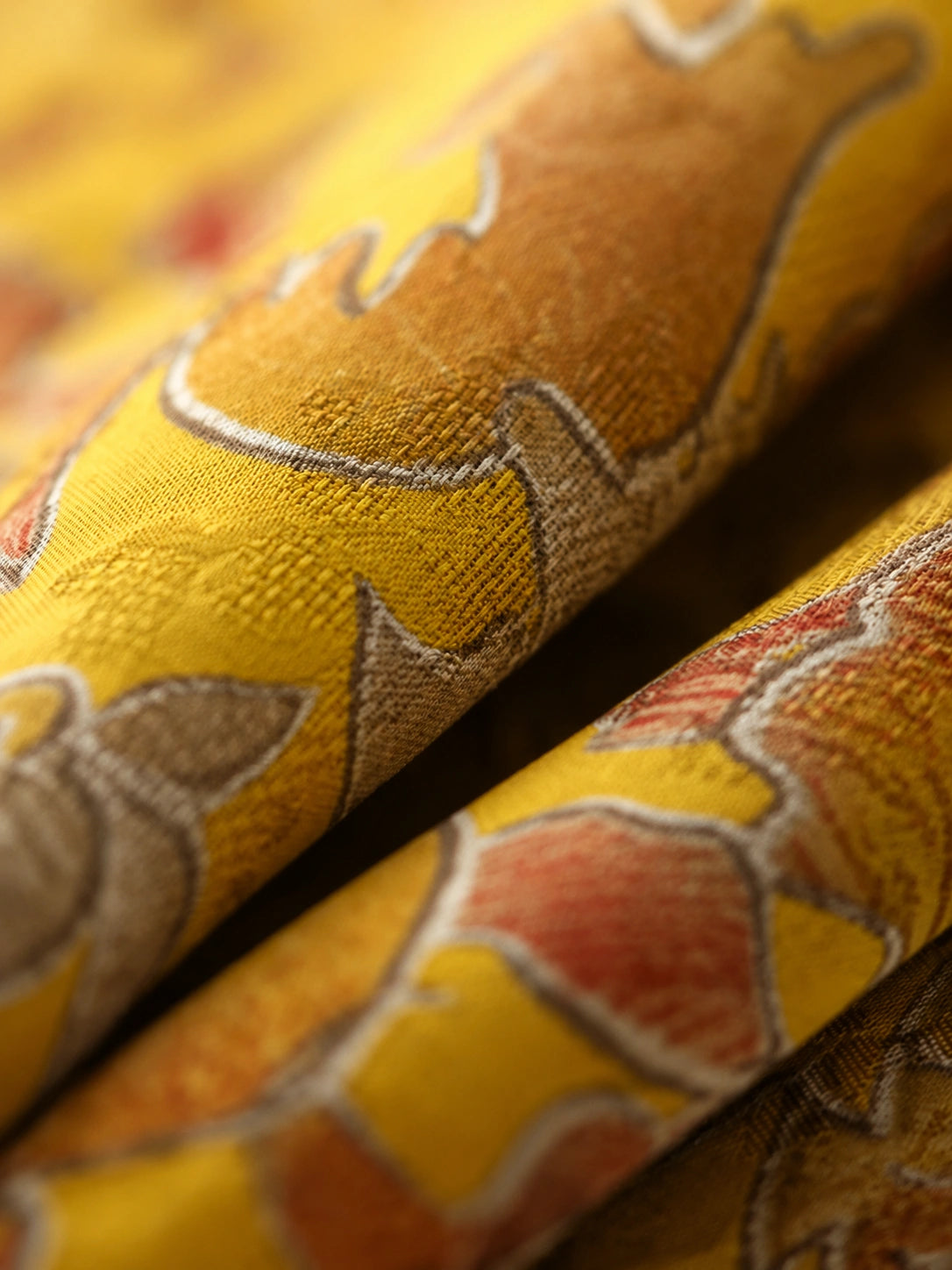 Close-up of golden satin-finish rayon fabric with textured botanical and auspicious animal motifs