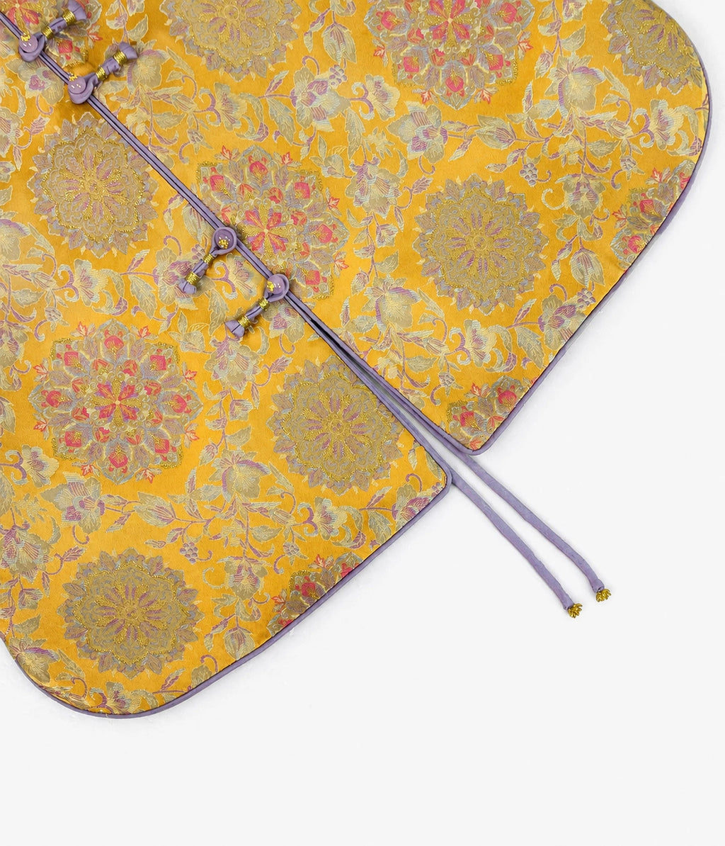Close-up of the saffron-gold floral brocade fabric, lavender frog buttons, curved hem and extended ties.