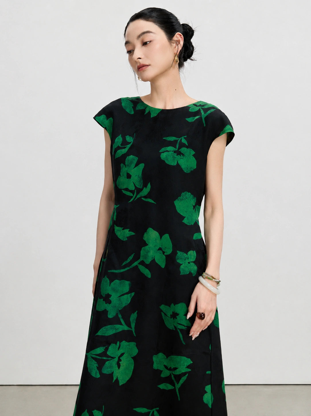 Three-quarter view of a New Chinese black silk dress with bold emerald botanical flowers.