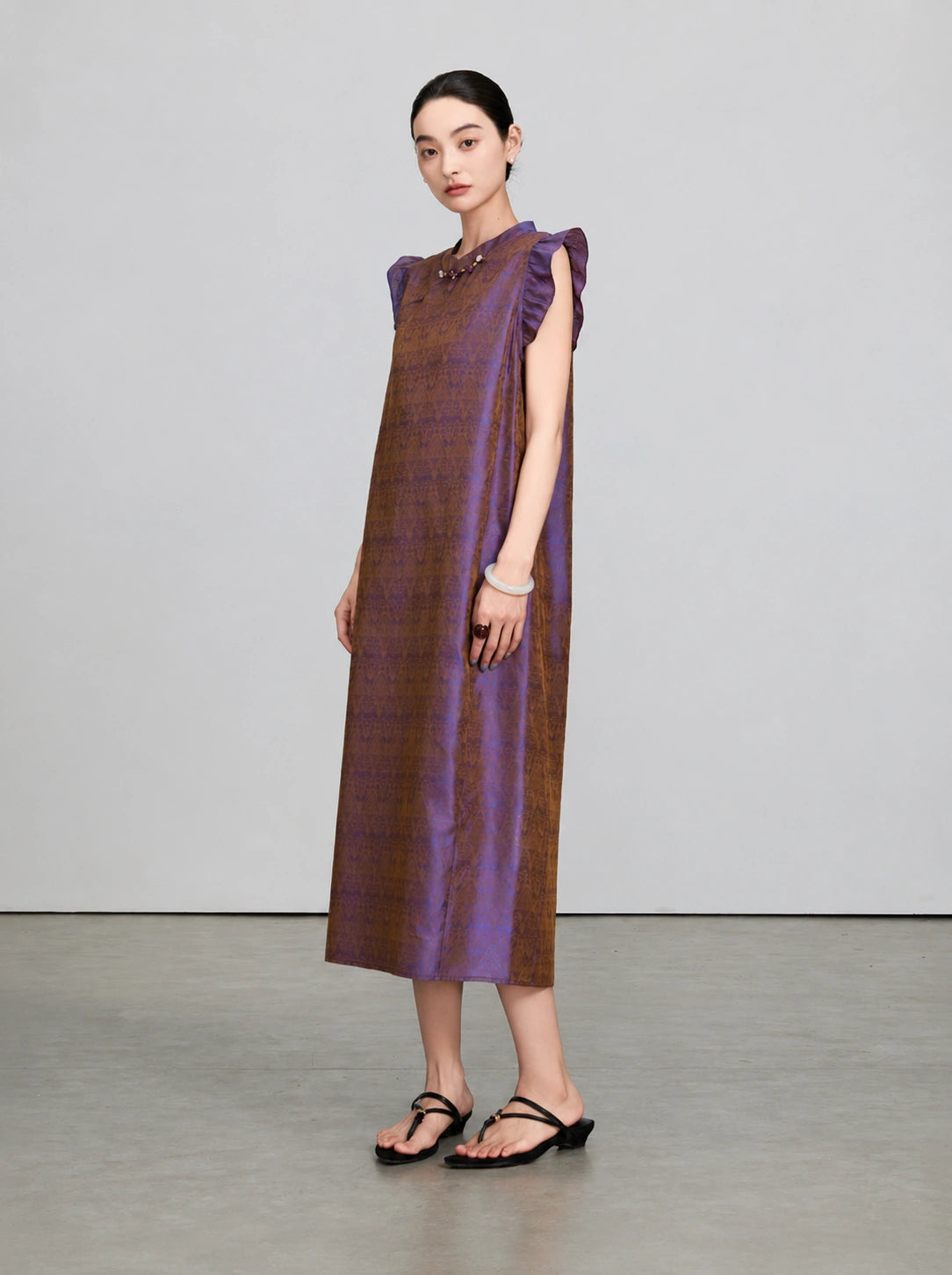 Front three-quarter view of an iridescent purple and bronze mulberry silk qipao dress with flutter sleeves.