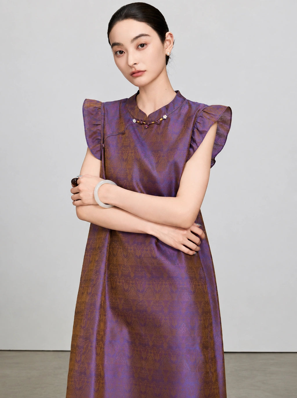 Portrait view of a woman wearing an iridescent purple and bronze New Chinese silk dress.