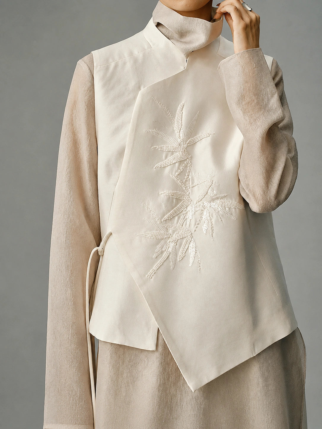 Close-up of tonal bamboo beadwork and the asymmetric front of an ivory wool and mulberry silk vest