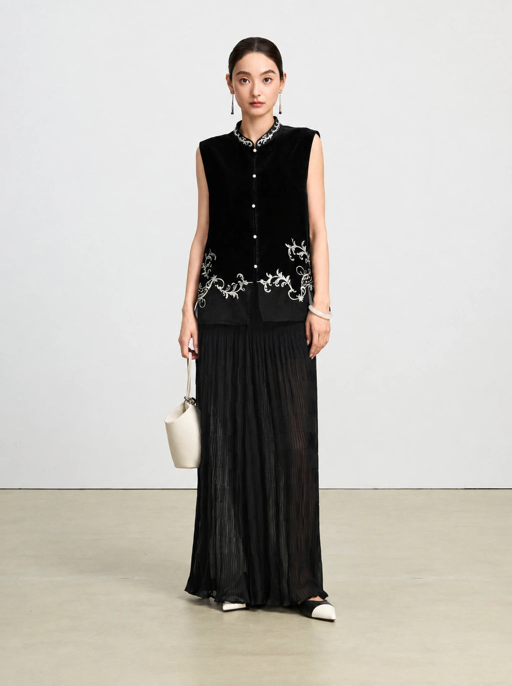 Front-facing model wearing a black silk velvet vest with ivory vine embroidery and sheer paneling.