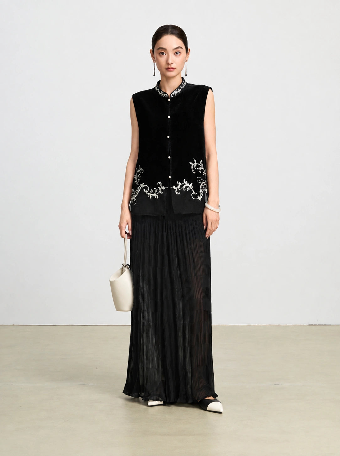Front-facing model wearing a black silk velvet vest with ivory vine embroidery and sheer paneling.