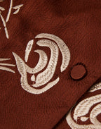 Close-up of ivory floral embroidery and a silk-covered button on rust-brown gambiered silk.