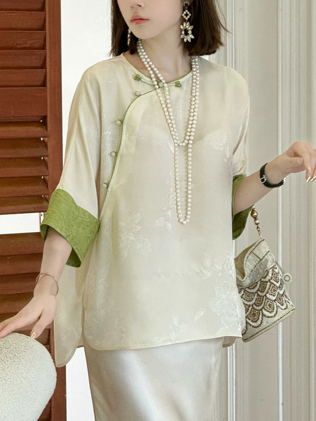 Model wearing an ivory silk top with Chinese-inspired detailing and contrasting green cuffs