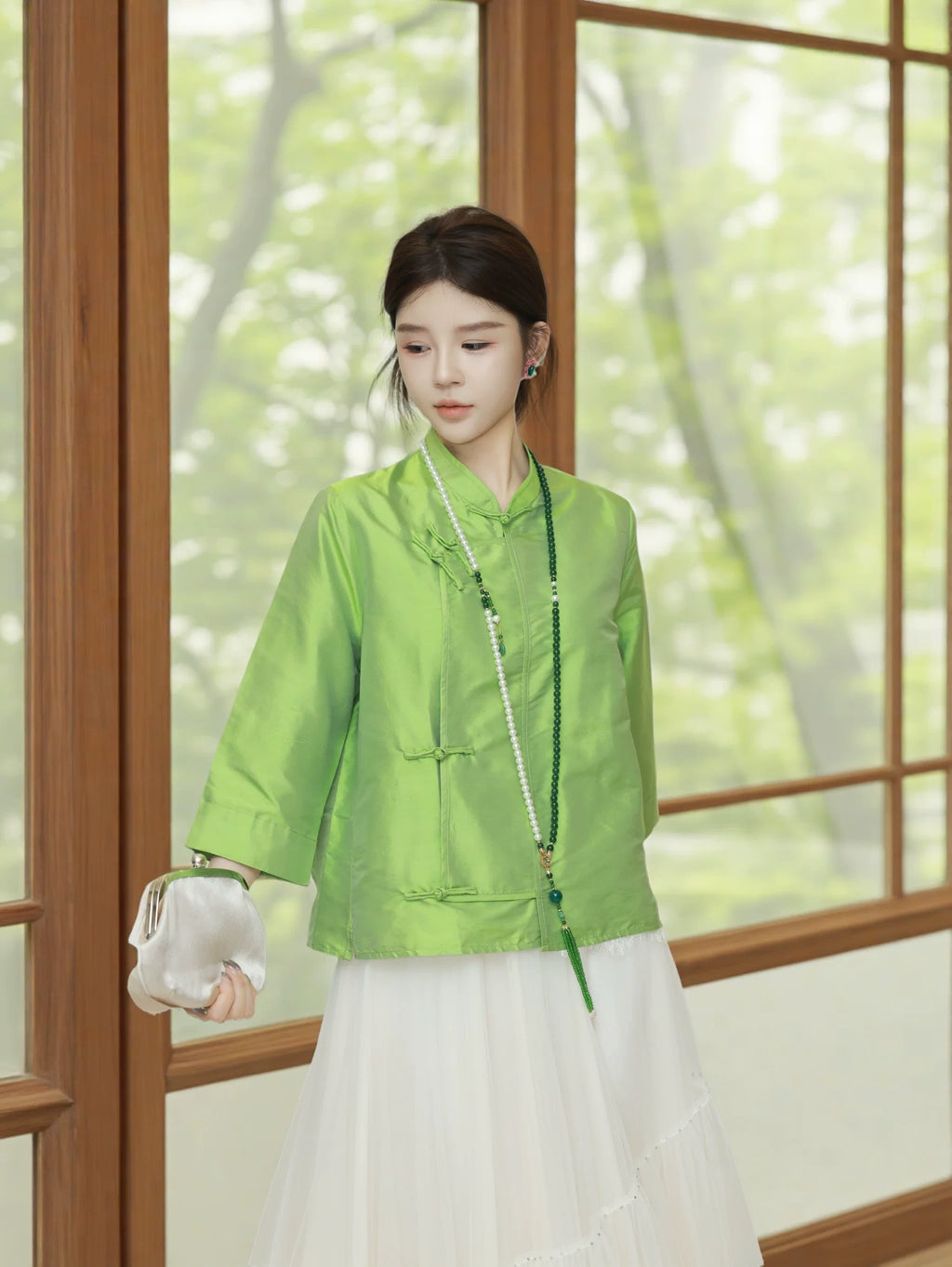 Model wearing a jade green silk top styled with a flowing white skirt and pearl necklace