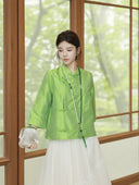 Model wearing a jade green silk top styled with a flowing white skirt and pearl necklace