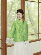 Model wearing a jade green silk top styled with a flowing white skirt and pearl necklace