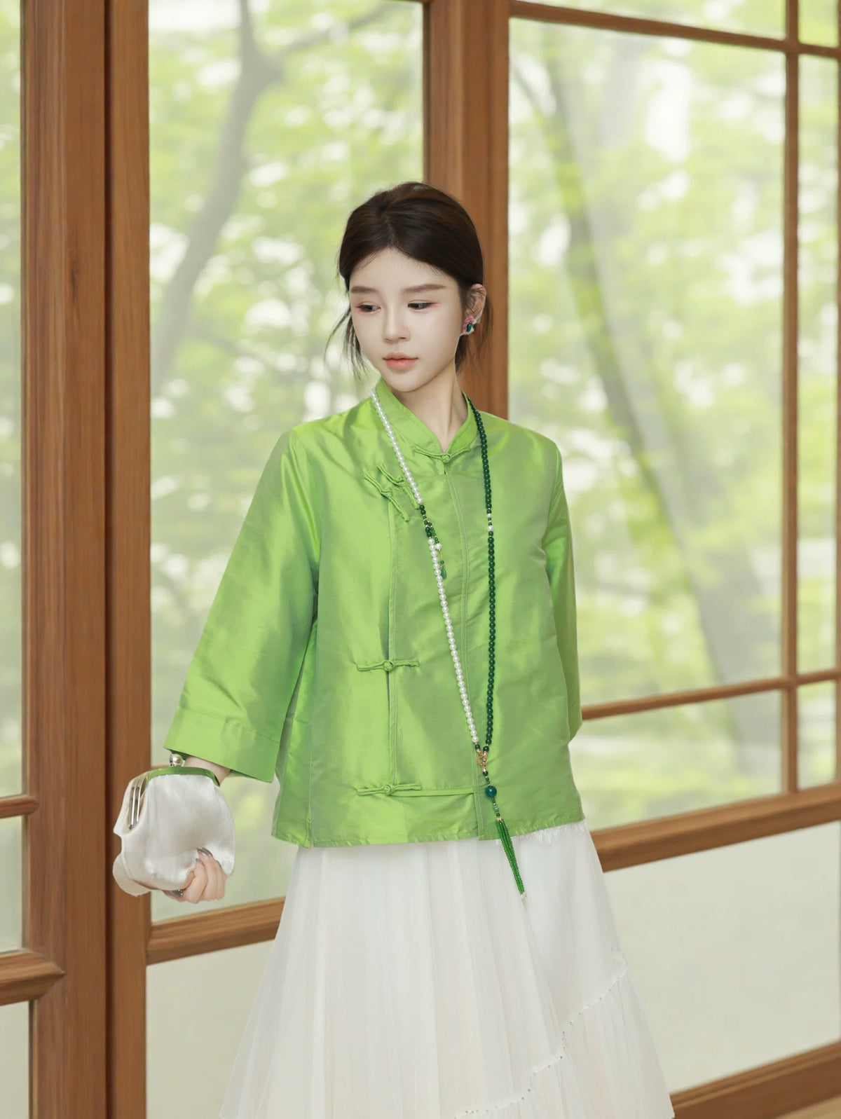 Model wearing a jade green silk top styled with a flowing white skirt and pearl necklace