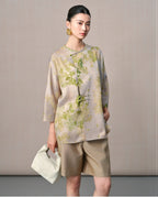 Model wearing a taupe and sage green leaf-print silk blouse with a round neckline and asymmetric button detail