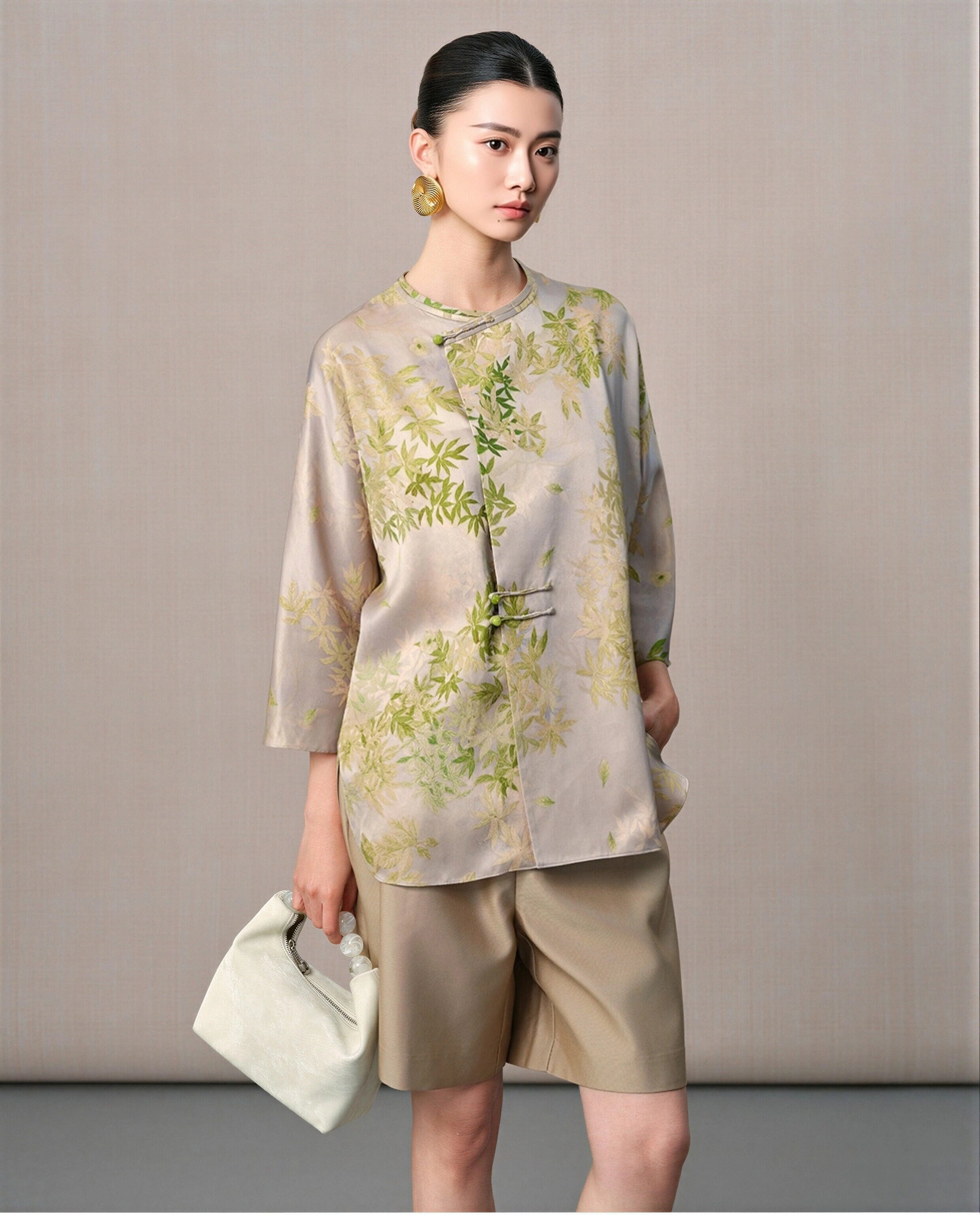 Model wearing a taupe and sage green leaf-print silk blouse with a round neckline and asymmetric button detail
