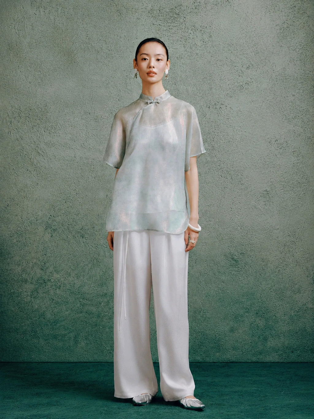Women's light celadon silk cheongsam top paired with wide-leg white trousers, styled in a modern Chinese-inspired outfit.