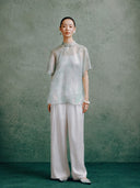 Women's light celadon silk cheongsam top paired with wide-leg white trousers, styled in a modern Chinese-inspired outfit.