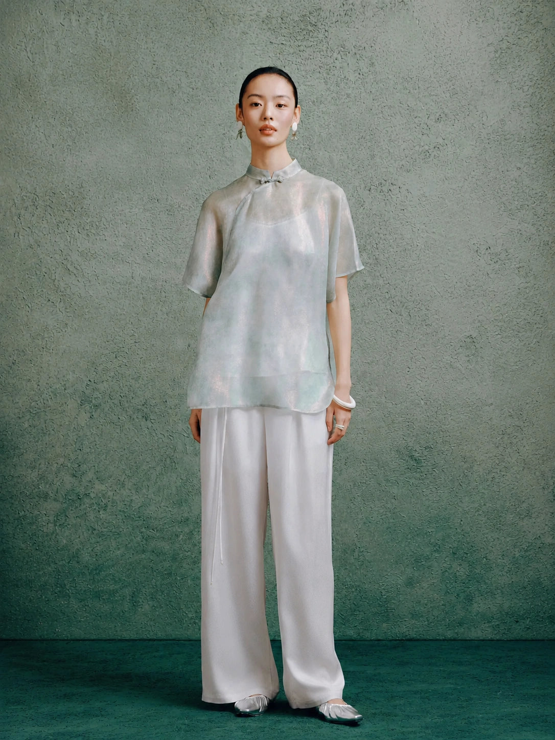 Women's light celadon silk cheongsam top paired with wide-leg white trousers, styled in a modern Chinese-inspired outfit.