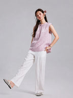 Model wearing a blush-lilac Gambiered Silk sleeveless top with white wide-leg trousers.
