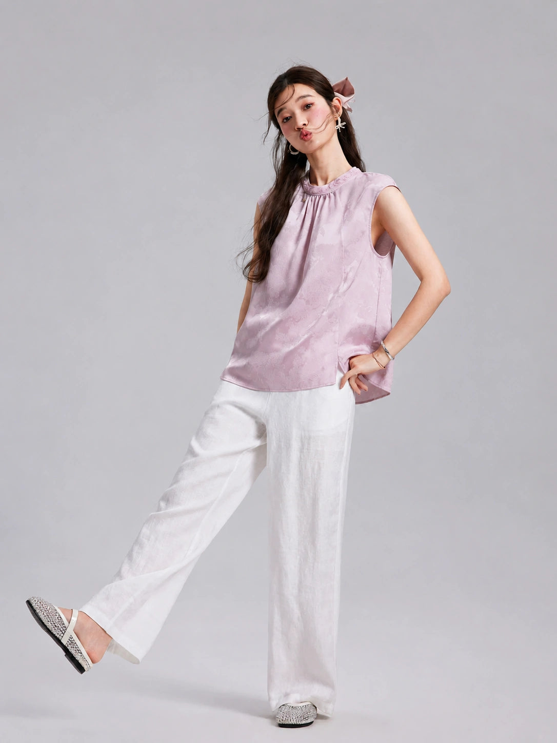 Model wearing a blush-lilac Gambiered Silk sleeveless top with white wide-leg trousers.