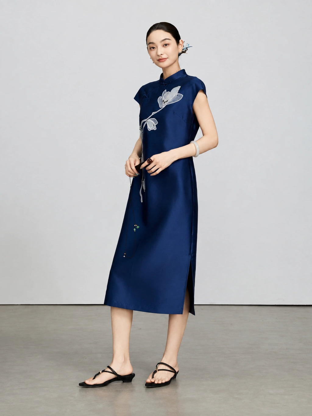 Model wearing a navy silk-wool qipao with white magnolia embroidery and a side slit