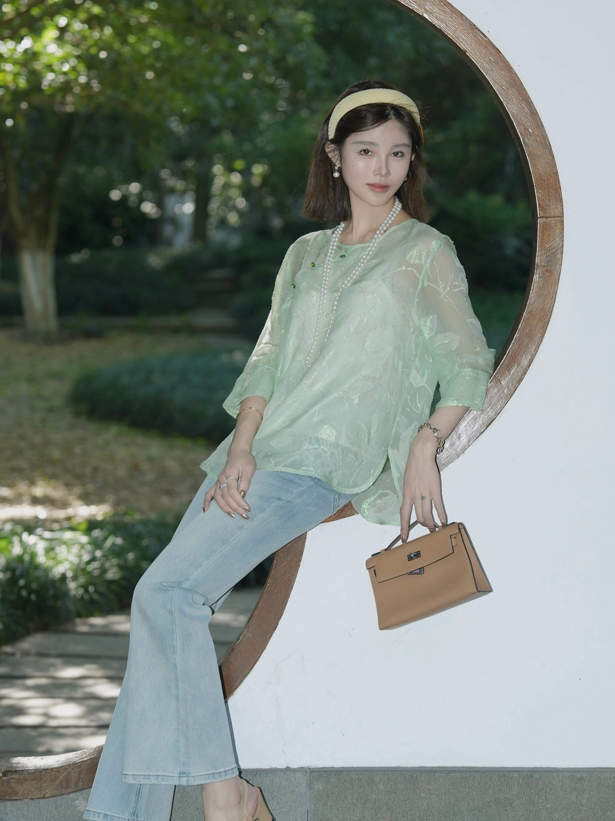 Model wearing a loose mint green silk top with jeans and a structured handbag outdoors