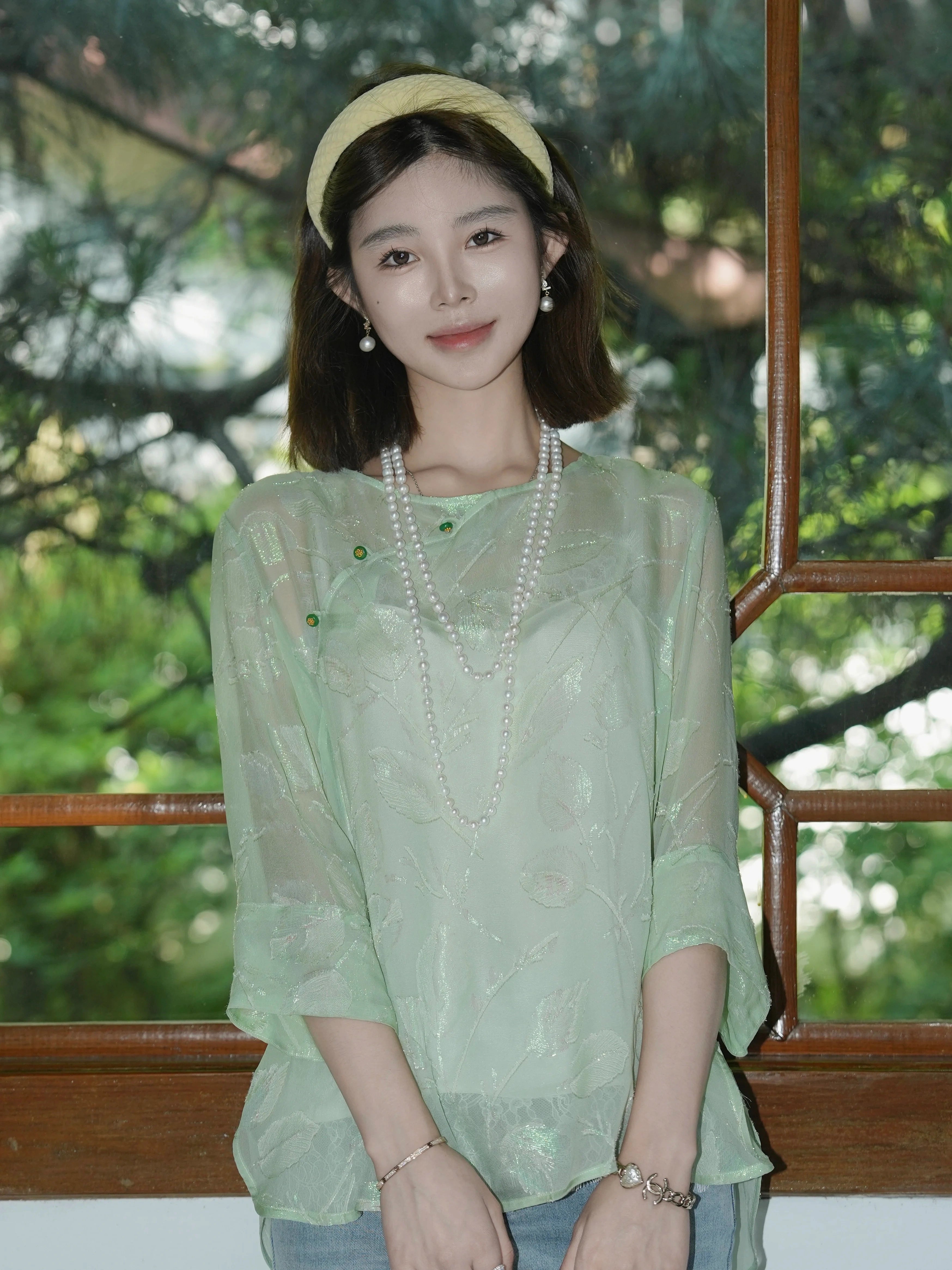 Model wearing a mint green textured silk top styled with layered pearl necklaces